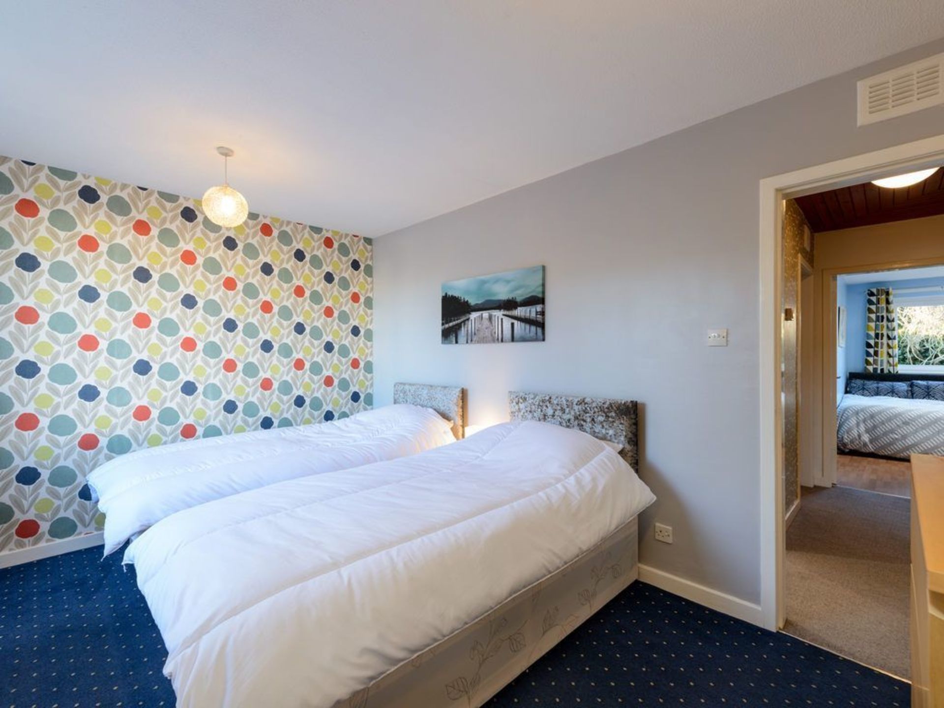 Une chambre à coucher avec un lit, un mur décoré d’un motif, un tableau et une vue sur une autre pièce.
