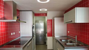 A compact kitchen with red tiled walls, stainless steel appliances, and a central island with a sink.