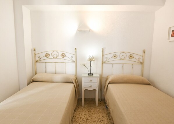 Ein Zimmer mit zwei Einzelbetten, einem Nachttisch mit Lampe und einer Wandleuchte.