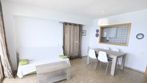Una habitació amb un llit, una taula de fusta amb cadires, una petita banca i un mirall a la paret.