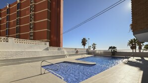 Una piscina amb un solàrium de rajoles, envoltada per una paret baixa i palmeres.