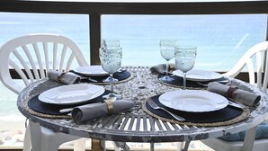 Taula rodona per a quatre persones, amb plats blancs, gots transparents i coberteria, amb vista a una platja.