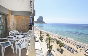 Ein Balkon mit Essplatz, der Blick auf einen Strand mit Sonnenschirmen und Palmen freigibt.