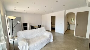 A spacious living area with a covered sofa, a dining table with chairs, a kitchen area, and a hallway leading to a bedroom. - Villenpark Playa Arena House Torre Isabel (Lloret de Mar)
