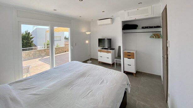 A modern bedroom with a large bed, a desk, a TV, and a wardrobe. - Villenpark Playa Arena House Torre Isabel (Lloret de Mar)