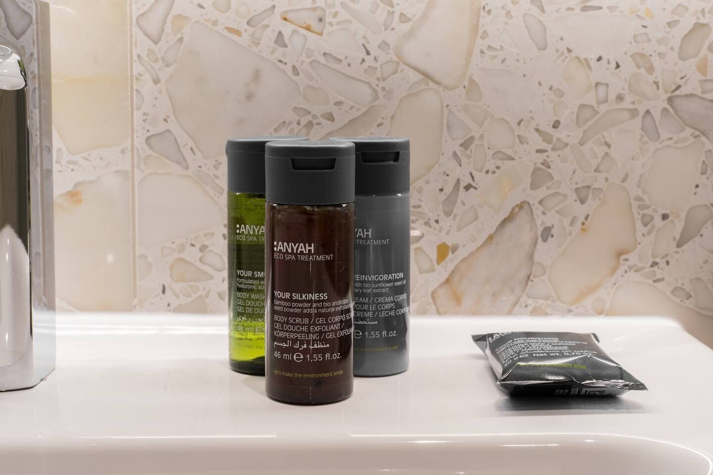 Three bottles of body wash and a packet of soap on a bathroom counter.