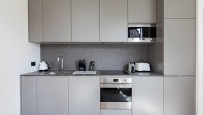 Eine moderne Küche mit grauen Schränken, einer Edelstahlspüle, einem Wasserkocher, einem Toaster und einer Mikrowelle.