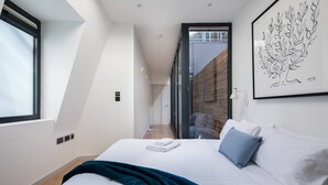 Ein modernes Hotelzimmer mit einem großen Bett, Blick durch eine Glastür und einem gerahmten Kunstwerk an der Wand.
