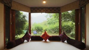 A room with a large bed, two windows, and a view of greenery.