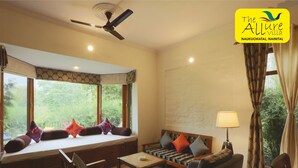 A hotel room with a large window, a ceiling fan, and a sofa with cushions.