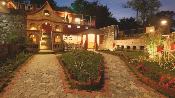 A two-story building with a stone facade, a balcony, and a paved entrance area with potted plants.