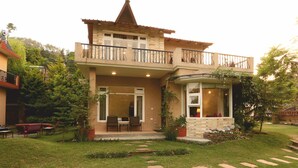 A two-story house with a balcony, a patio with outdoor furniture, and a well-maintained garden.