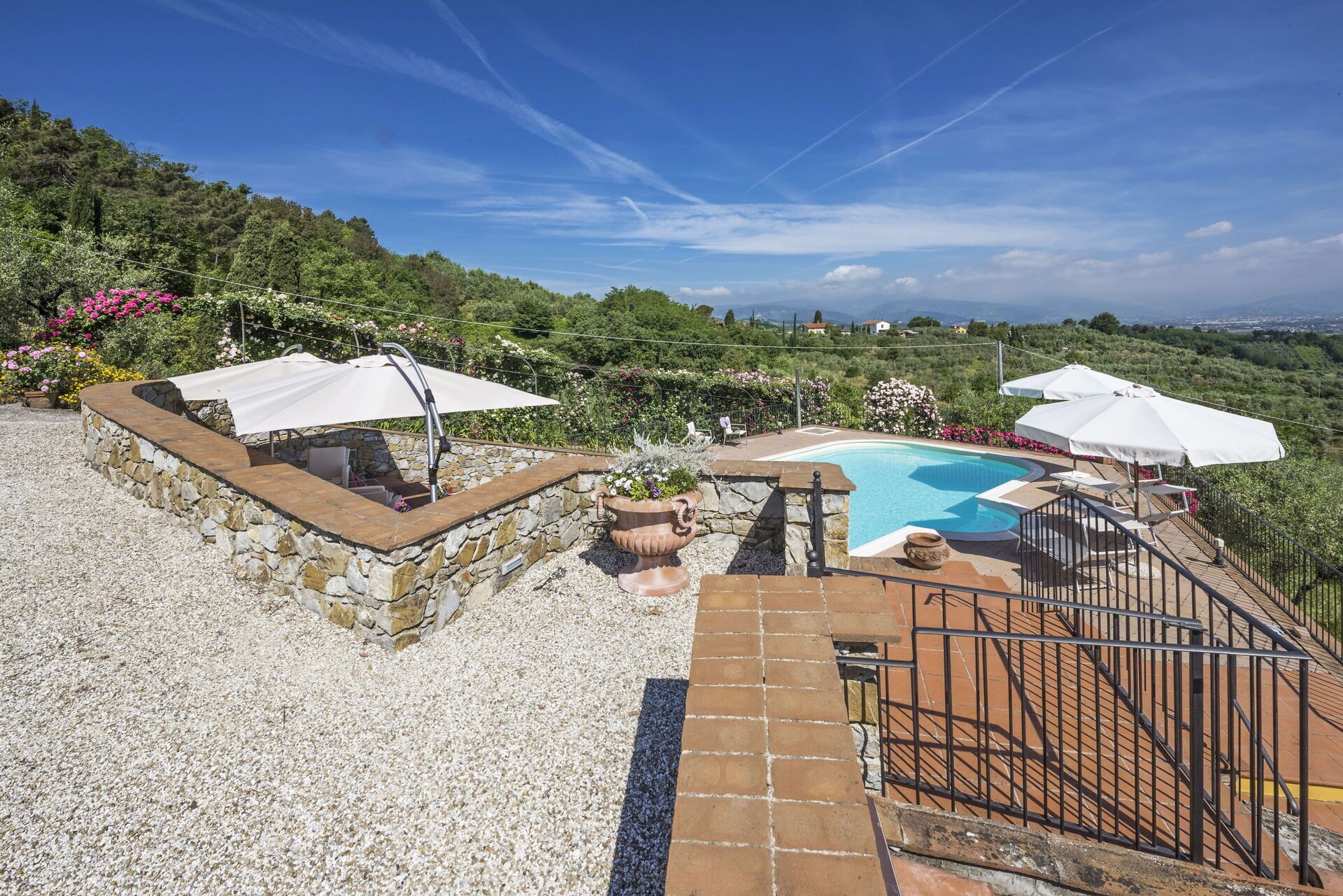 A pool area with stone walls, white umbrellas, and a view of the countryside.