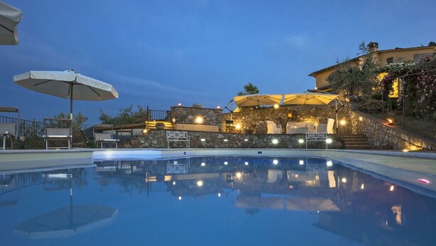 A swimming pool with a stone wall and outdoor seating area, surrounded by a building with a stone facade and a staircase leading to a higher level.