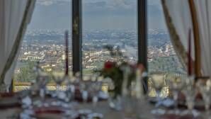 A dining table with glasses and a vase, set against a view of a town and mountains.
