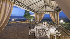 An outdoor dining area with a table set for two, overlooking a cityscape at dusk.