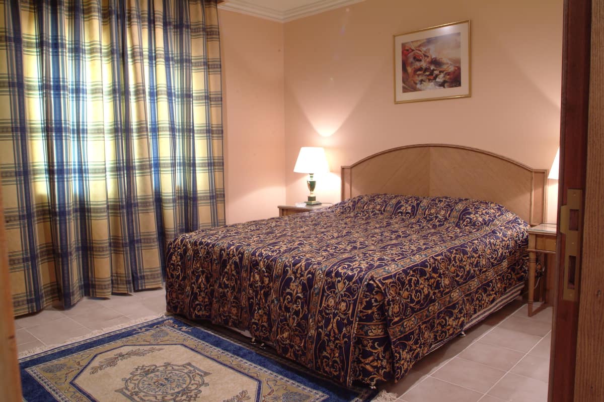 Une chambre d’hôtel avec un grand lit, une table de chevet avec une lampe, un tableau au mur et un rideau à carreaux.