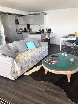 Cozy living space with a sofa, coffee table, and dining area, featuring a kitchen with sink and cabinets.
