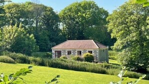 Een stenen huis met een schuin dak, omgeven door weelderige begroeiing en bomen.