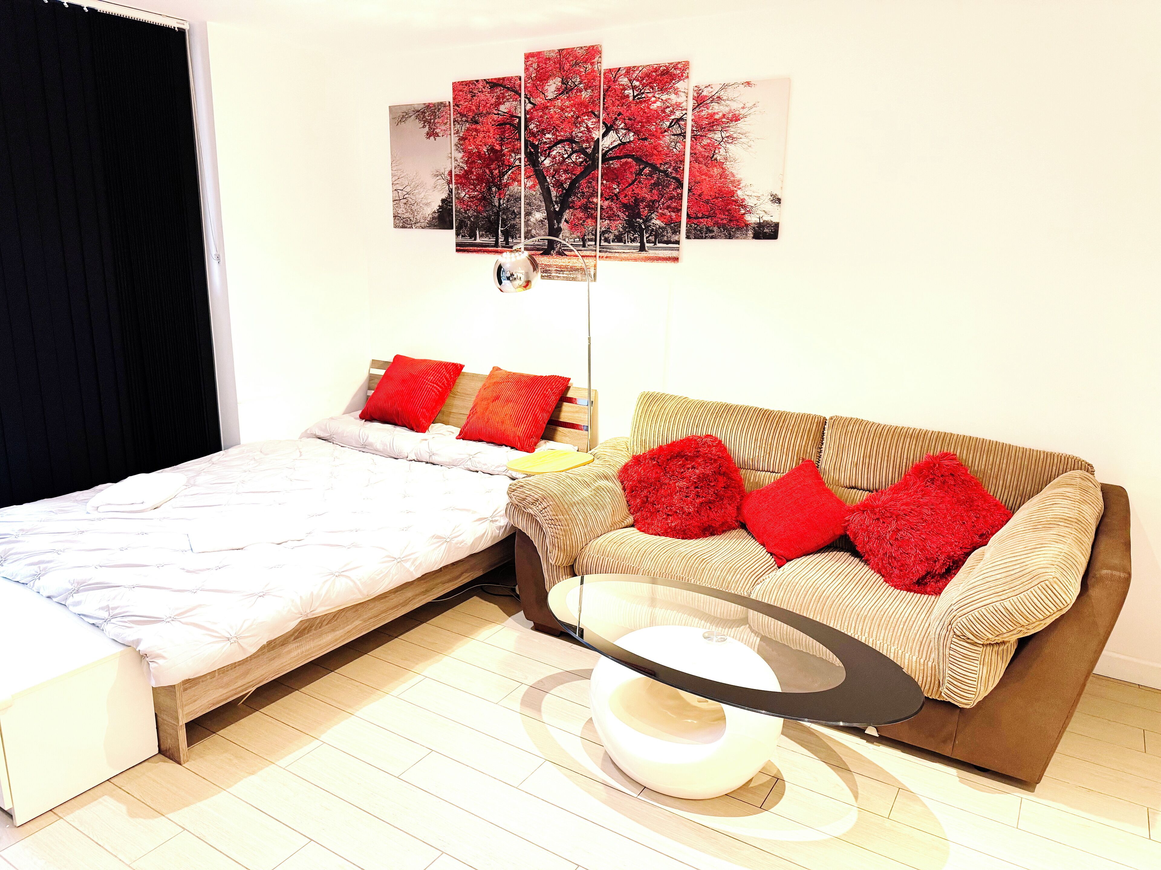 A bedroom with a bed, a sofa, a coffee table, and a wall-mounted picture of a tree.