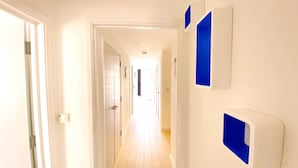 Ein Flur mit weißen Wänden, Holzboden und einer Tür links. Auf der rechten Wand befinden sich drei blaue Wandobjekte.