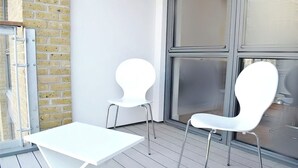 Ein moderner Außenbereich mit einem weißen Tisch und zwei weißen Stühlen, einer Ziegelwand und einem großen Fenster.