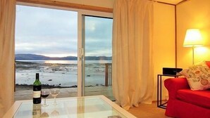 Una habitación con una mesa de vidrio, un sofá rojo, una lámpara y vistas a la playa y las montañas.