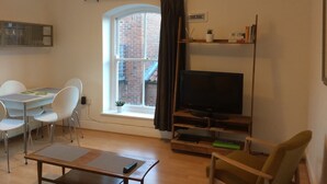 A living room with a dining table, chairs, a TV, and a window with a view of a brick building.