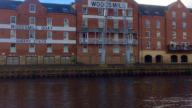 A waterfront building with signs reading "Woodsmill Quay" and "Queens Stait."