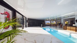 En moderne indendørs swimmingpool med frit udsyn til det omkringliggende område, inklusive et spiseområde og en reception.