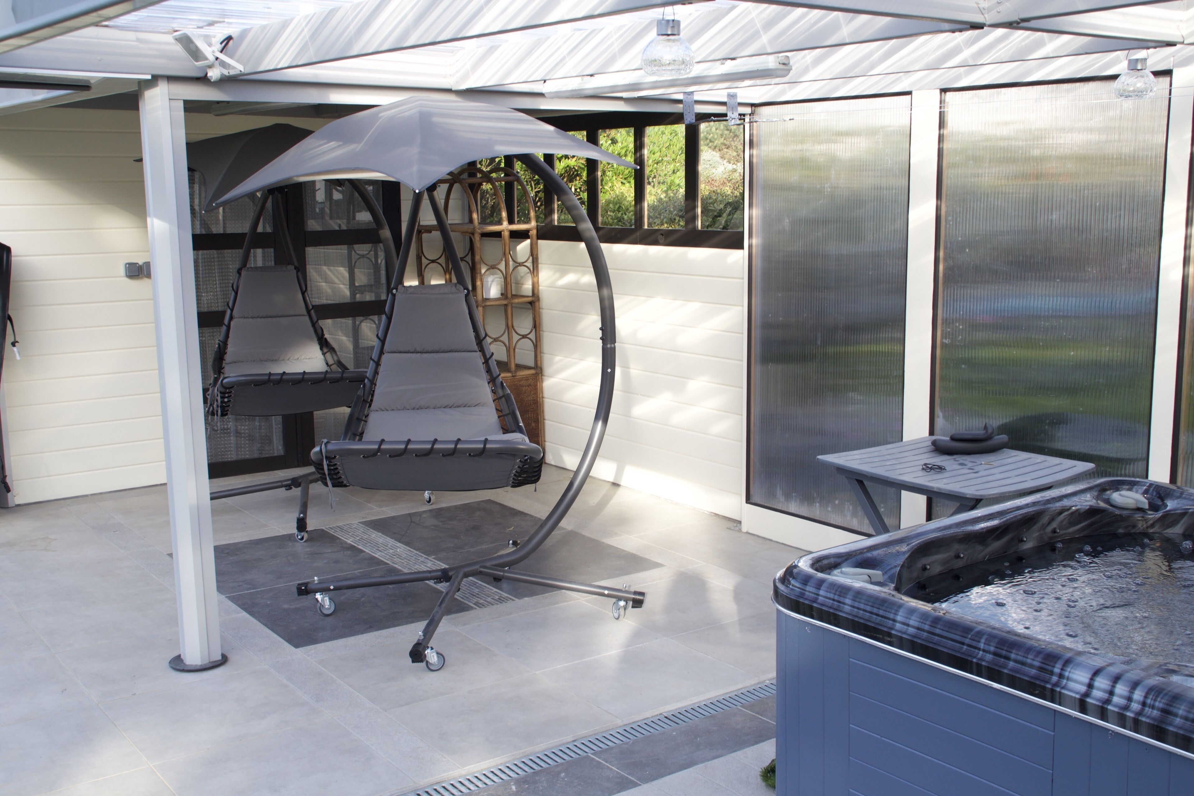 Une terrasse couverte avec un jacuzzi, une chaise suspendue et une table.