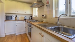 Et køkken med hvide skabe, en stålvask, en mikrobølgeovn, en brødrister og en komfur.