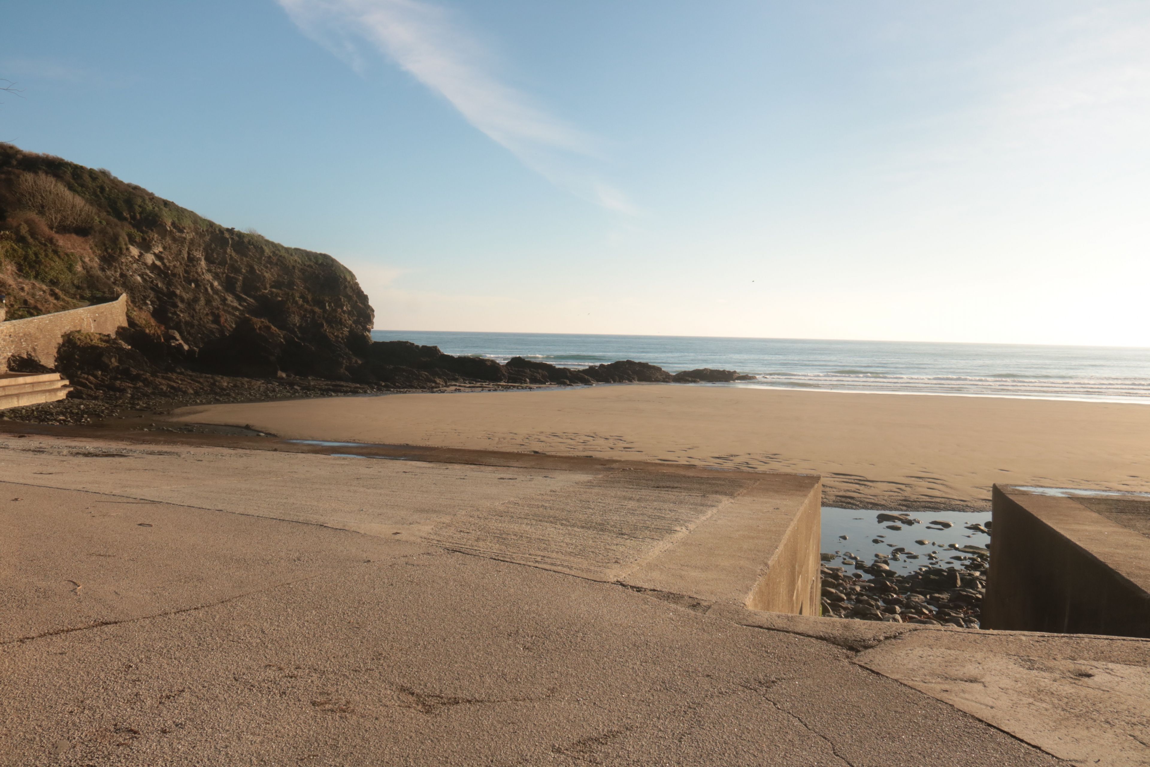 A coastal beach with a concrete walkway and rocky outcrops.