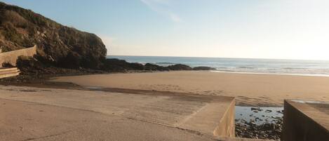 A coastal beach with a concrete walkway and rocky outcrops.