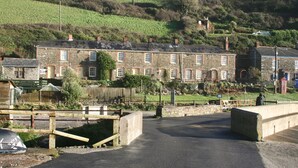 A stone building with multiple windows and a paved entrance area. - Wonderful reverse level conversion located on the sea front in picturesque rural hamlet on the South (Saint Austell)
