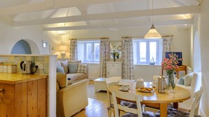 A cozy living room with a sofa, a dining table with chairs, a kitchen area with a kettle, and a TV. - Wonderful reverse level conversion located on the sea front in picturesque rural hamlet on the South (Saint Austell)