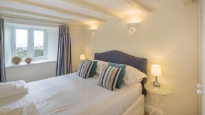 A neatly made bed with striped pillows, a bedside lamp, and a window with curtains. - Wonderful reverse level conversion located on the sea front in picturesque rural hamlet on the South (Saint Austell)