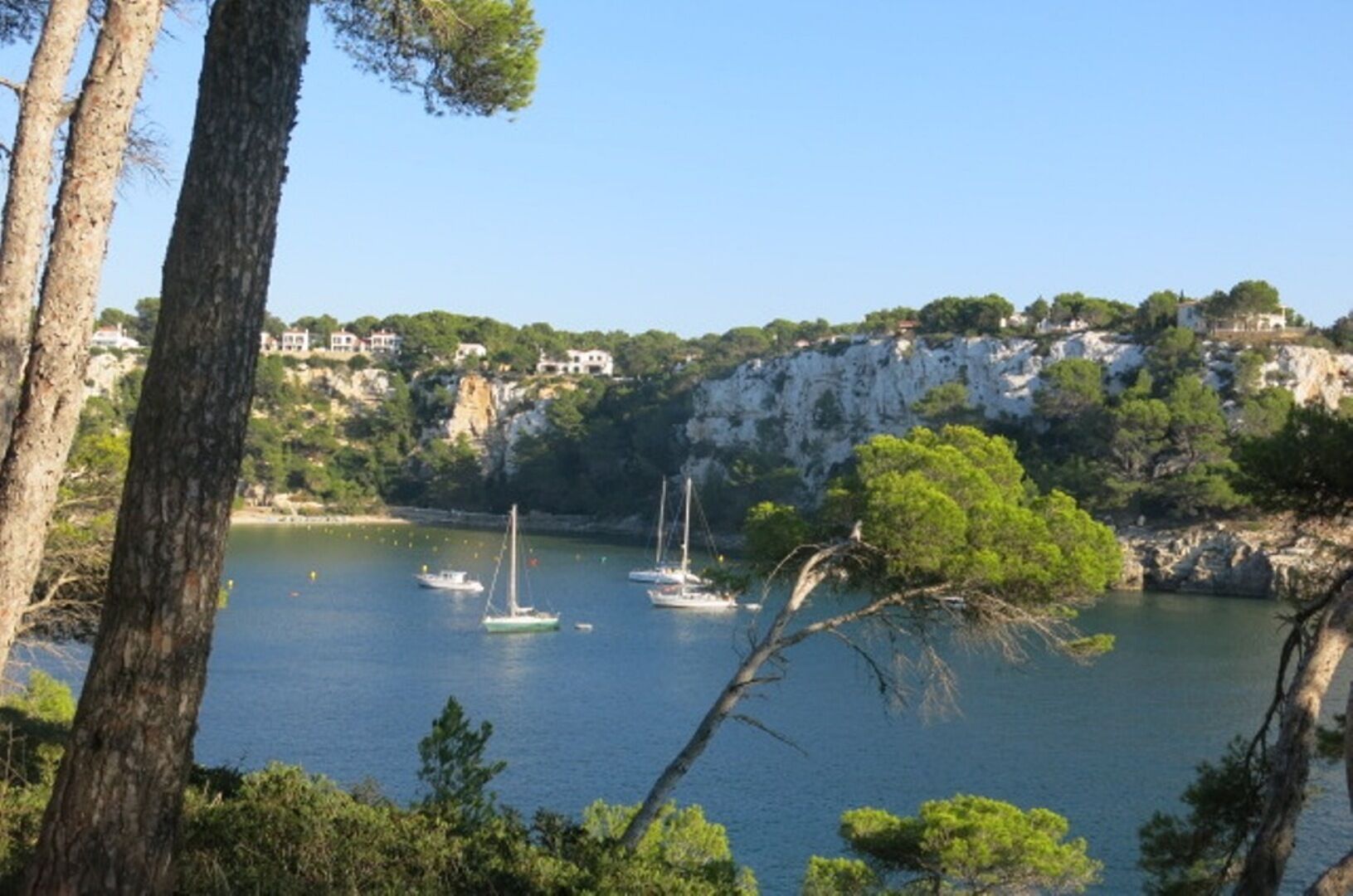 A coastal scene with boats on calm water, surrounded by cliffs and trees.