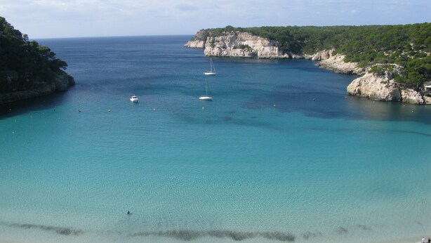 A coastal beach with clear turquoise waters, boats, and rocky cliffs. - Nice apartment with sea views Son bou (Son Bou Minorca)