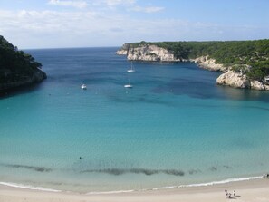 Une plage côtière aux eaux turquoise et limpides, avec des bateaux et des falaises rocheuses.