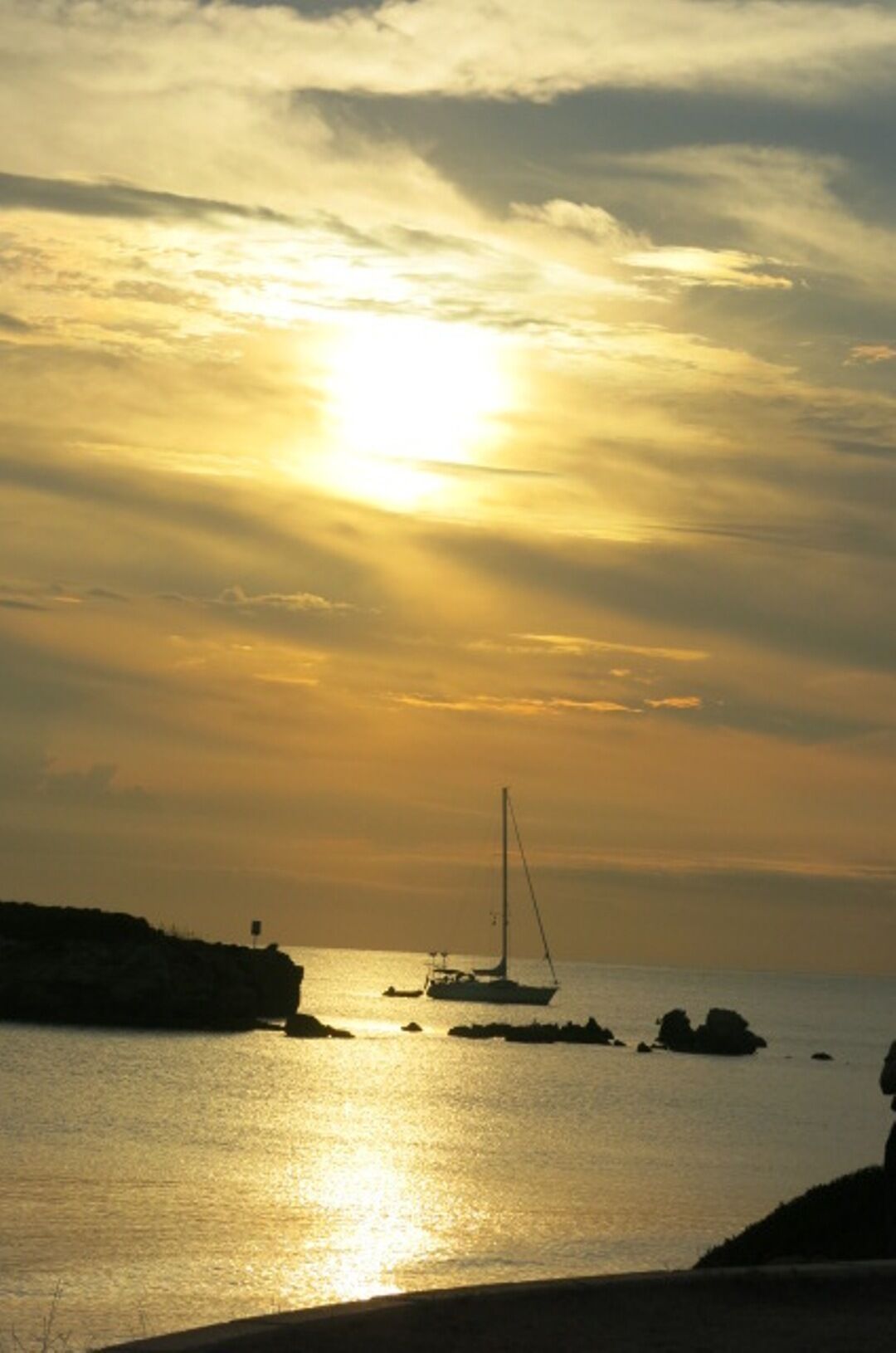 Ein Sonnenuntergang über einem ruhigen Meer mit einem Segelboot und einer felsigen Küstenlinie.