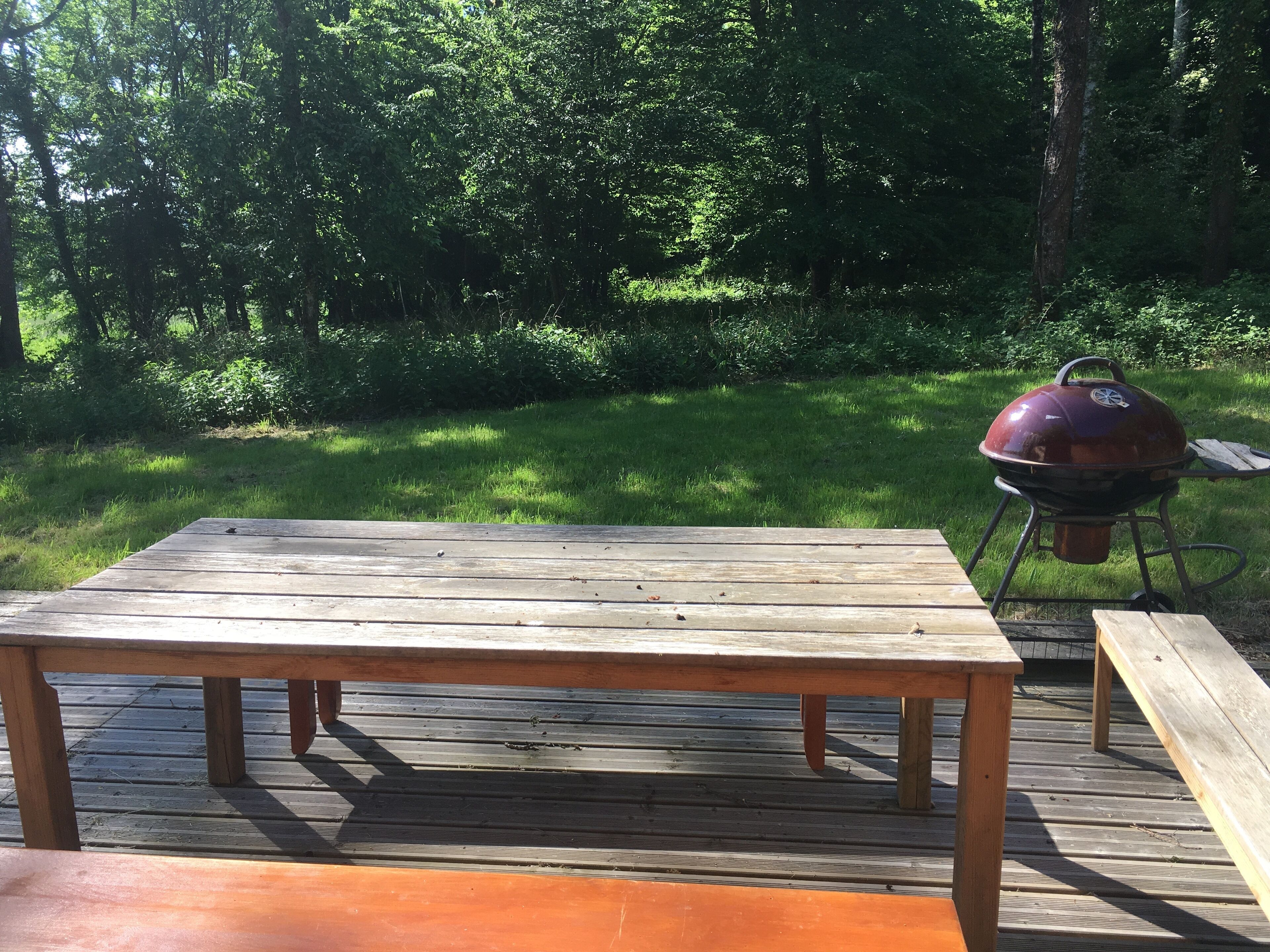 A wooden deck with a table and a barbecue grill.