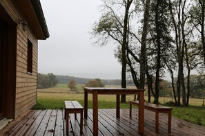 A wooden deck with a table and benches overlooking a grassy field and trees. - comfortable and cozy cottage in the countryside (Vendeuvre-Sur-Barse)