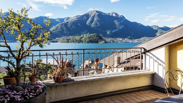 A balcony with potted plants, a view of a lake, and mountains in the background.