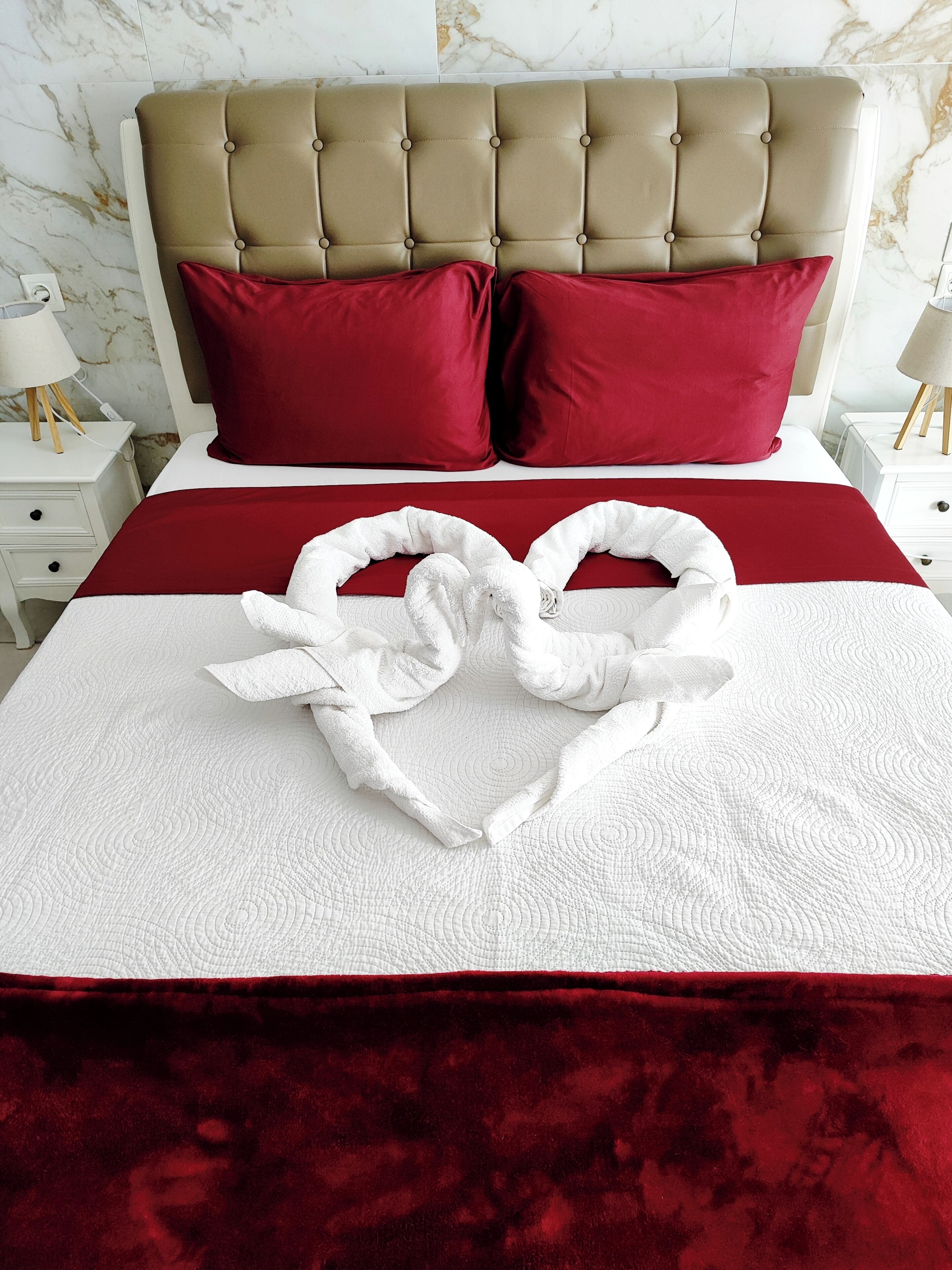 Een bed met een rood-witte dekbedovertrek, twee rode kussens en een handdoek in de vorm van een hart.