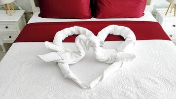 Een bed met een rood-witte dekbedovertrek, twee rode kussens en een handdoek in de vorm van een hart.