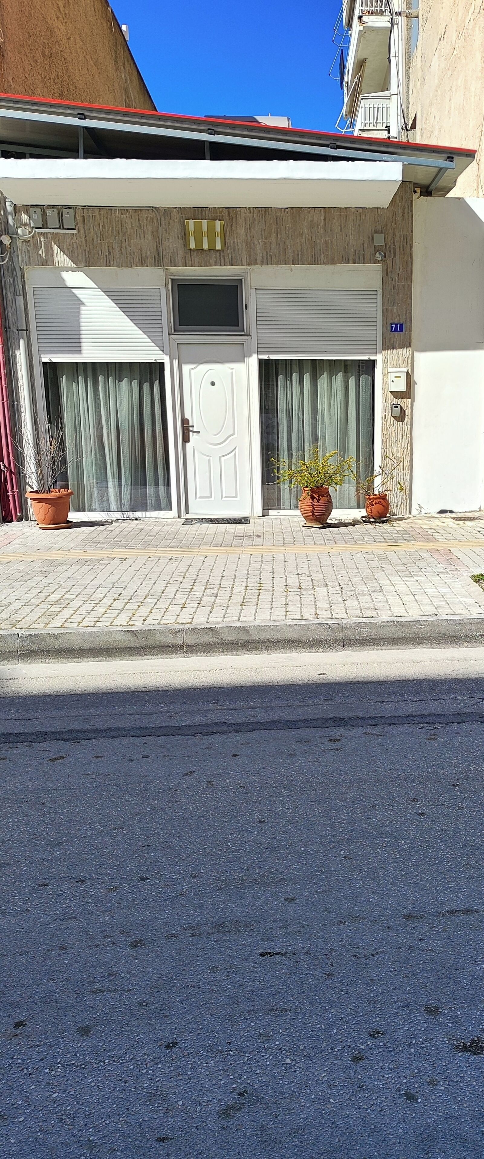 Un bâtiment avec une porte de garage fermée, un pot de fleurs et un panneau portant le numéro « 71 ».