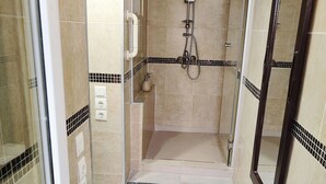 Un espacio de ducha pequeño con azulejos, una puerta de cristal, un tapete blanco y suelo de azulejos.