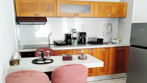 Una cocina con gabinetes de madera, un refrigerador de acero inoxidable, una encimera blanca y dos taburetes rosas.