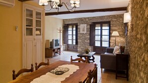 A dining area with a wooden table, chairs, a chandelier, and a stone wall in the background. - Rural house with pool and jacuzzi (Can Llobet - Canigó) (Capmany)